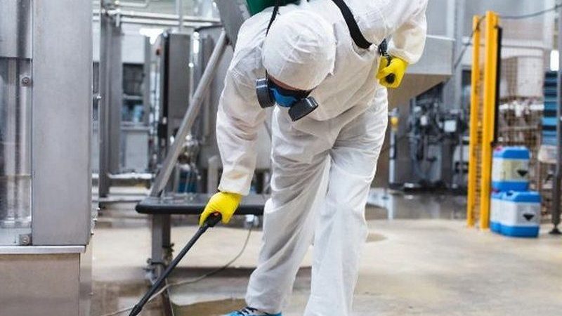 Técnico con equipo de protección tratando el suelo de una planta alimentaria