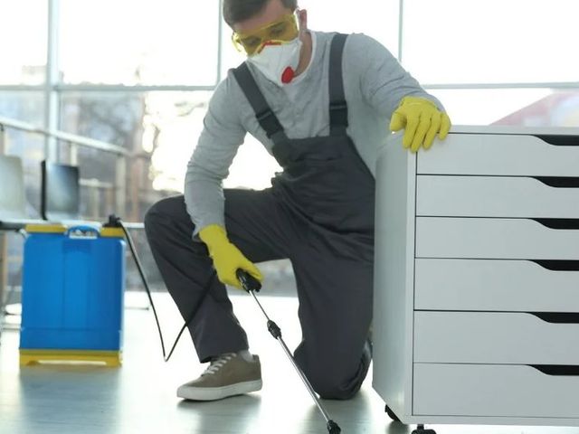 Técnico con mascarilla aplicando desinfectante junto a un mueble de cajones