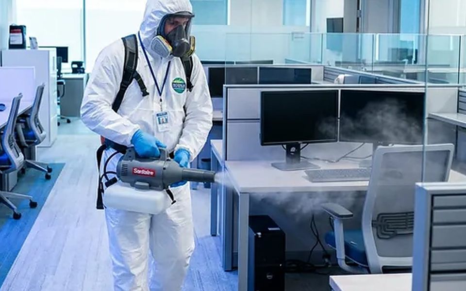 Dos técnicos con buzo integral nebulizando desinfectante en una estancia