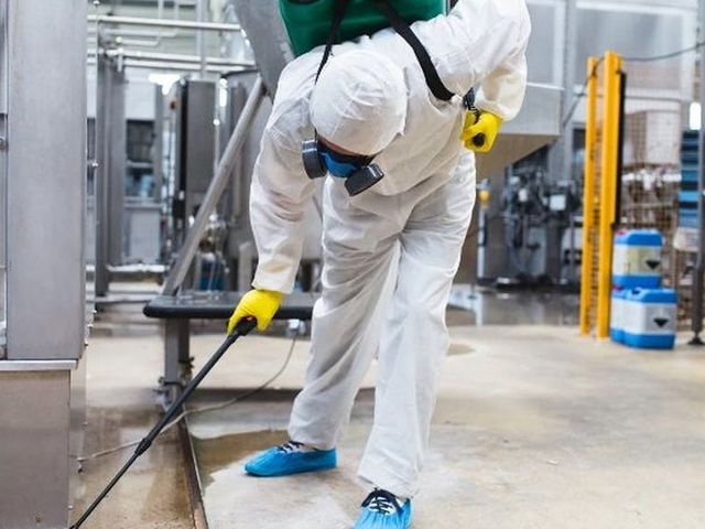 Técnico con EPI tratando el suelo de una planta alimentaria