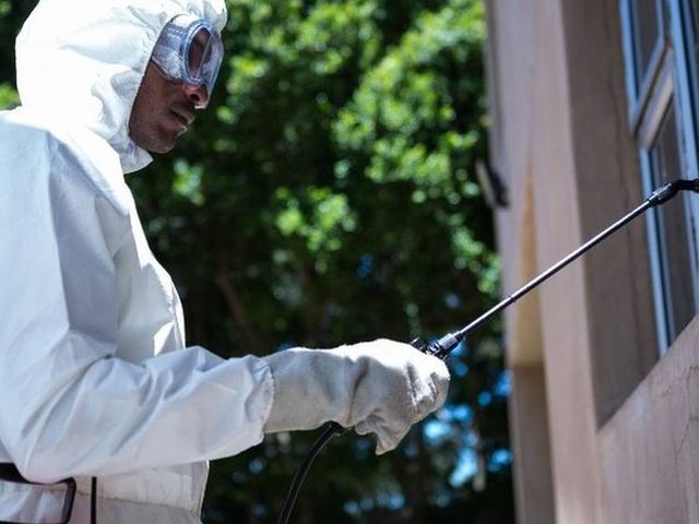 Técnico con buzo y gafas aplicando tratamiento en el exterior de una vivienda