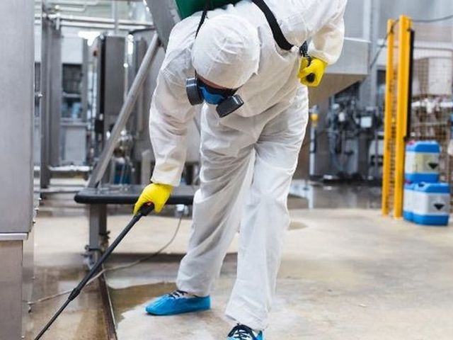 Técnico con EPI desinfectando el suelo de una instalación industrial