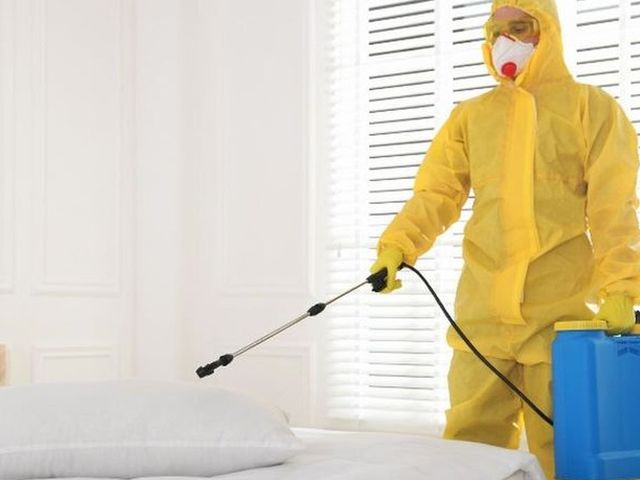 Técnico con buzo tratando textiles y cama con pulverizador